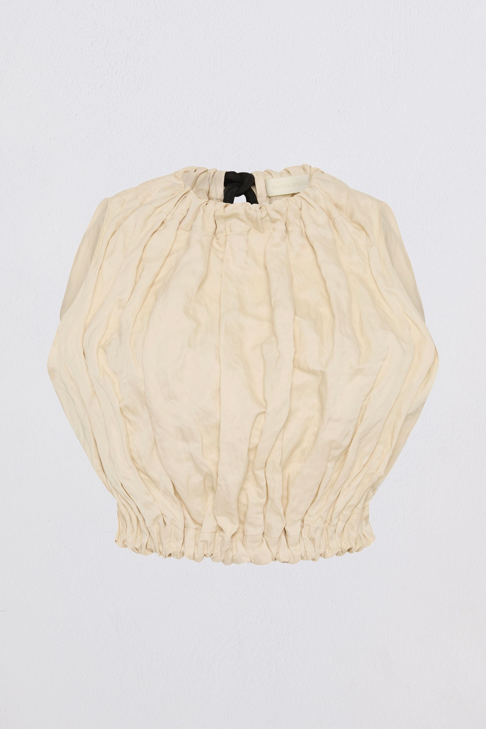 A cream-colored, crinkled cotton blouse with voluminous balloon sleeves and a gathered elastic hem, laid flat against a light gray background.