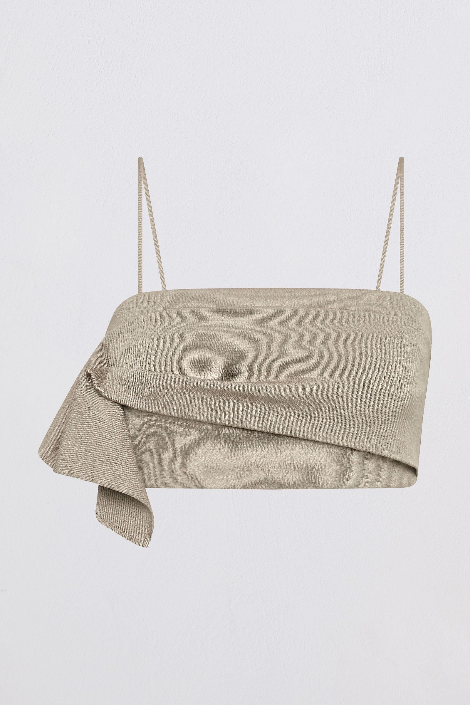 A light beige asymmetrical draped tube top with thin spaghetti straps, shown against a plain white background.