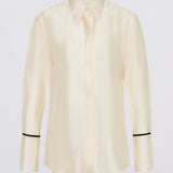A cream-colored long-sleeve button-up shirt with black piping trim on the cuffs, displayed against a light gray background.