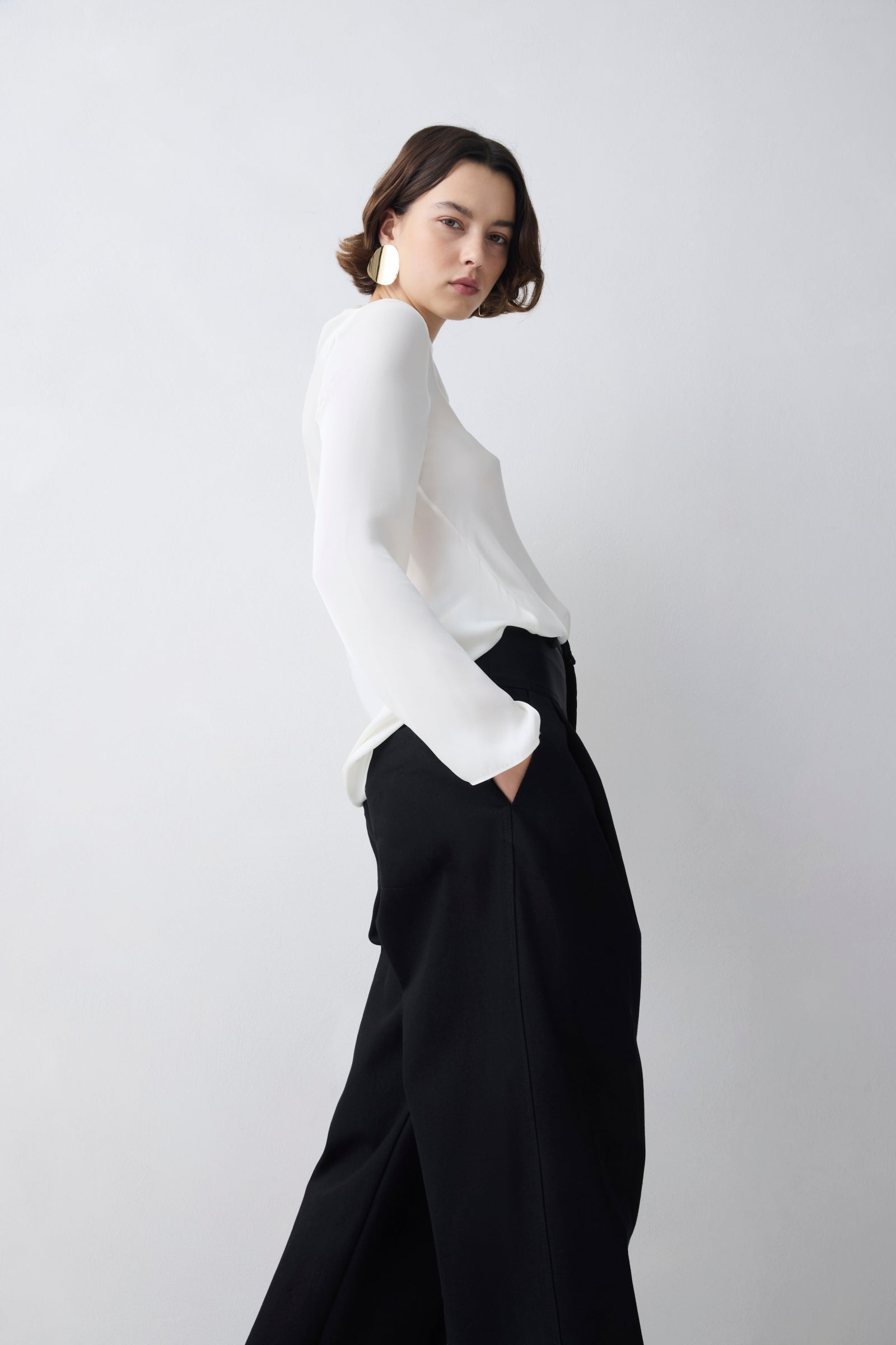 Woman wearing a white blouse and black pants against a plain background
