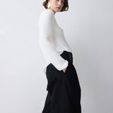 Woman wearing a white blouse and black pants against a plain background