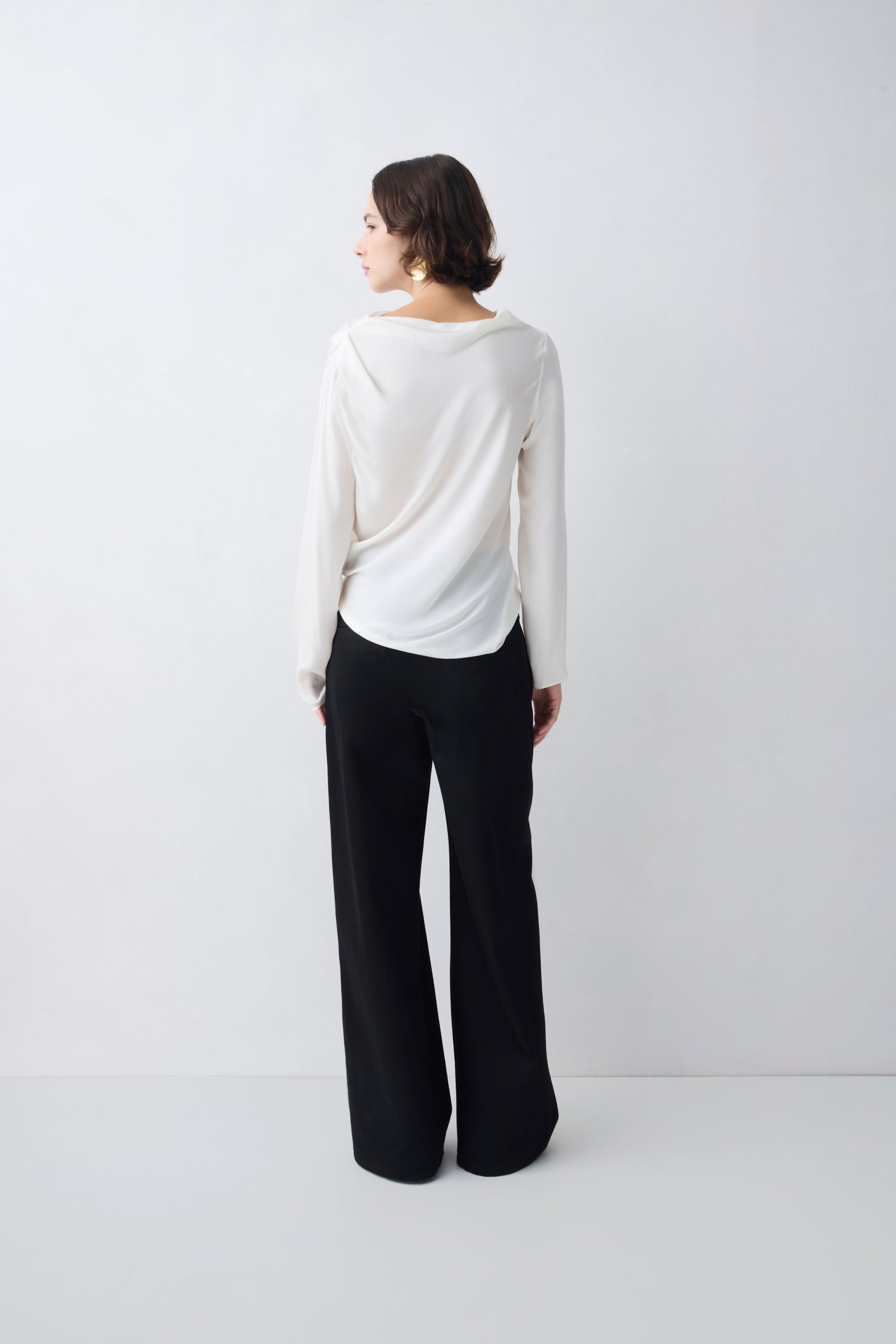 Woman wearing a white long-sleeve top and black wide-leg pants on a white background