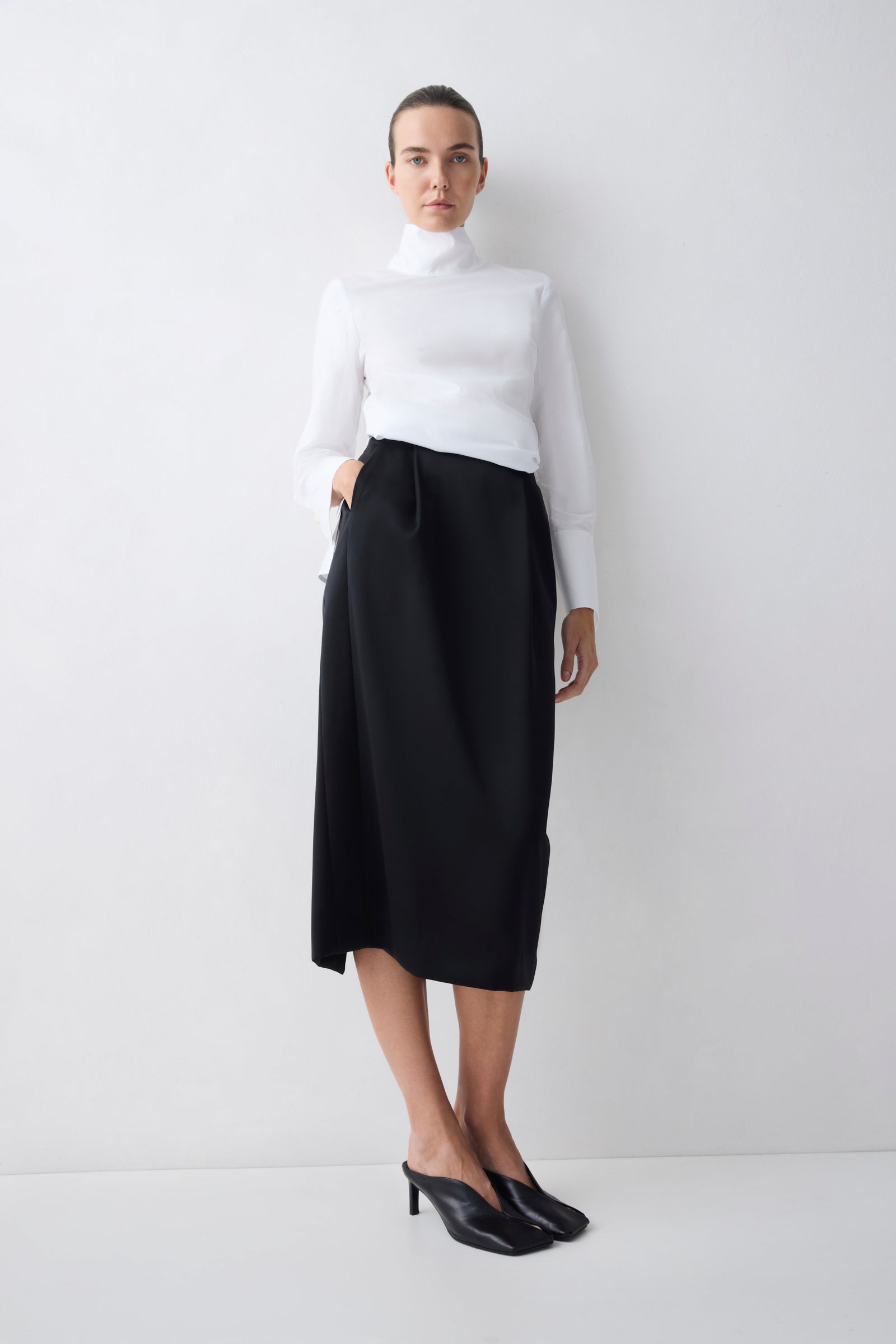 Woman wearing a white turtleneck and black skirt on a white background