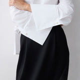 White blouse with ruffled sleeves and black skirt on a plain background