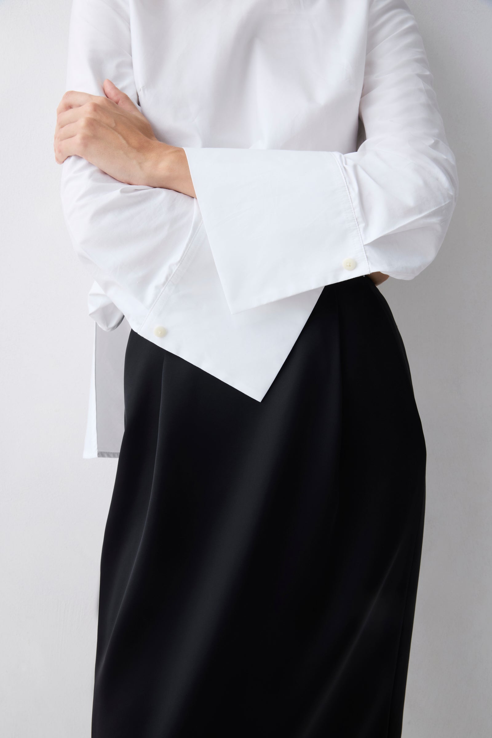 White blouse with ruffled sleeves and black skirt on a plain background