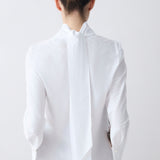 Person wearing a white blouse with a high collar on a plain background