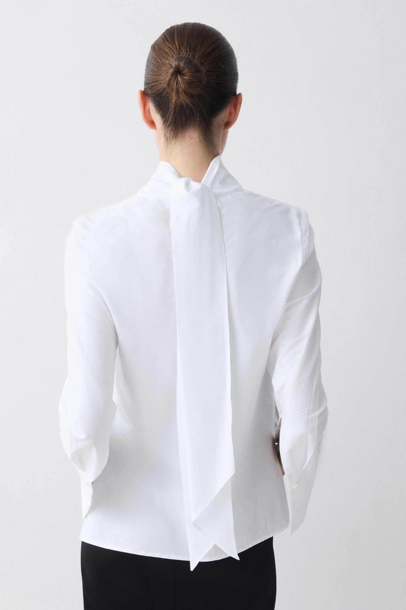 Person wearing a white blouse with a high collar on a plain background