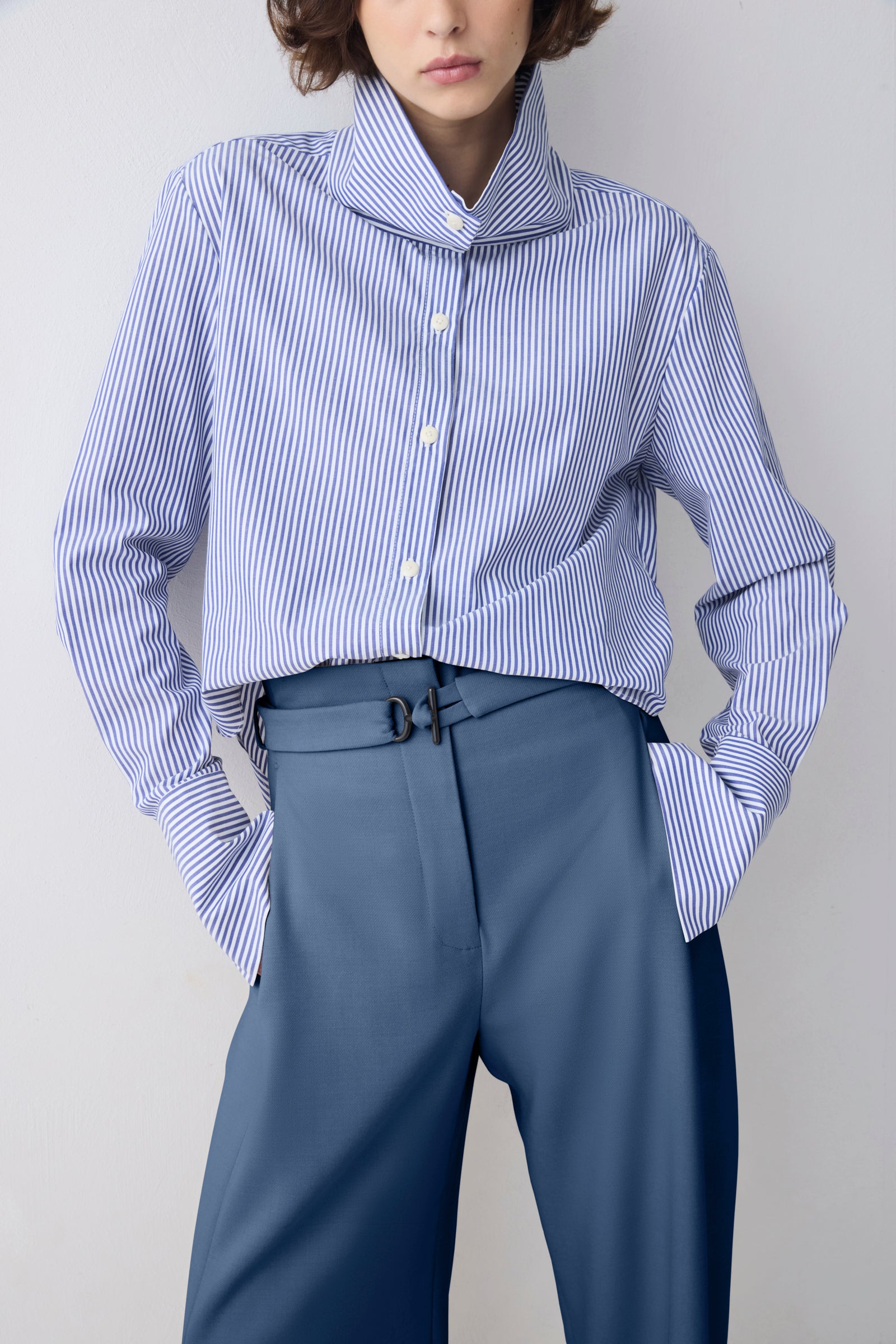 Person wearing a blue and white striped shirt with a high collar and blue pants on a plain background