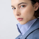Woman wearing a gray coat over a striped shirt on a light gray background