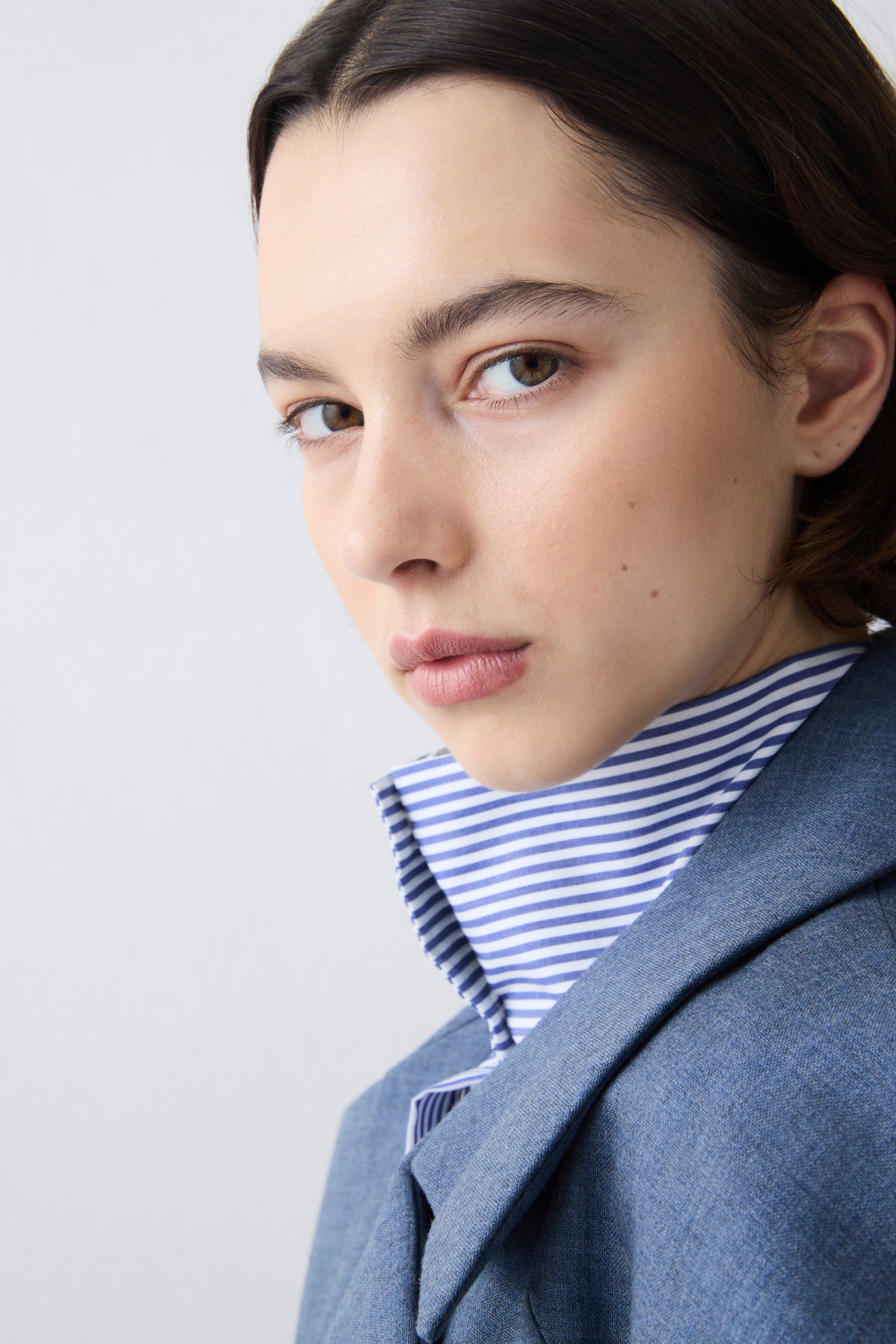 Woman wearing a gray coat over a striped shirt on a light gray background