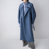 Person wearing a long blue coat on a plain background