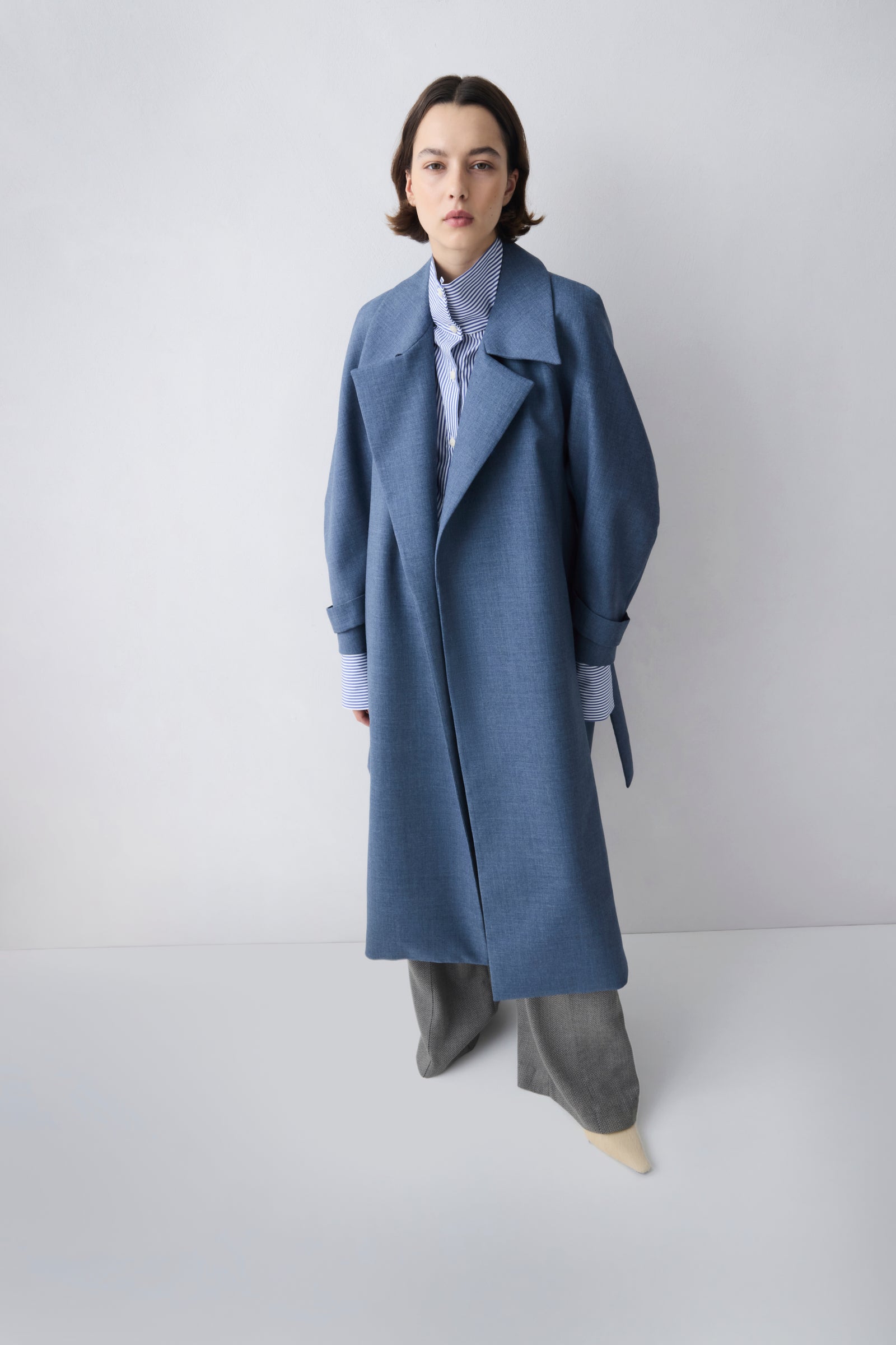 Person wearing a long blue coat on a plain background