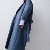 Person wearing a long blue coat on a plain background