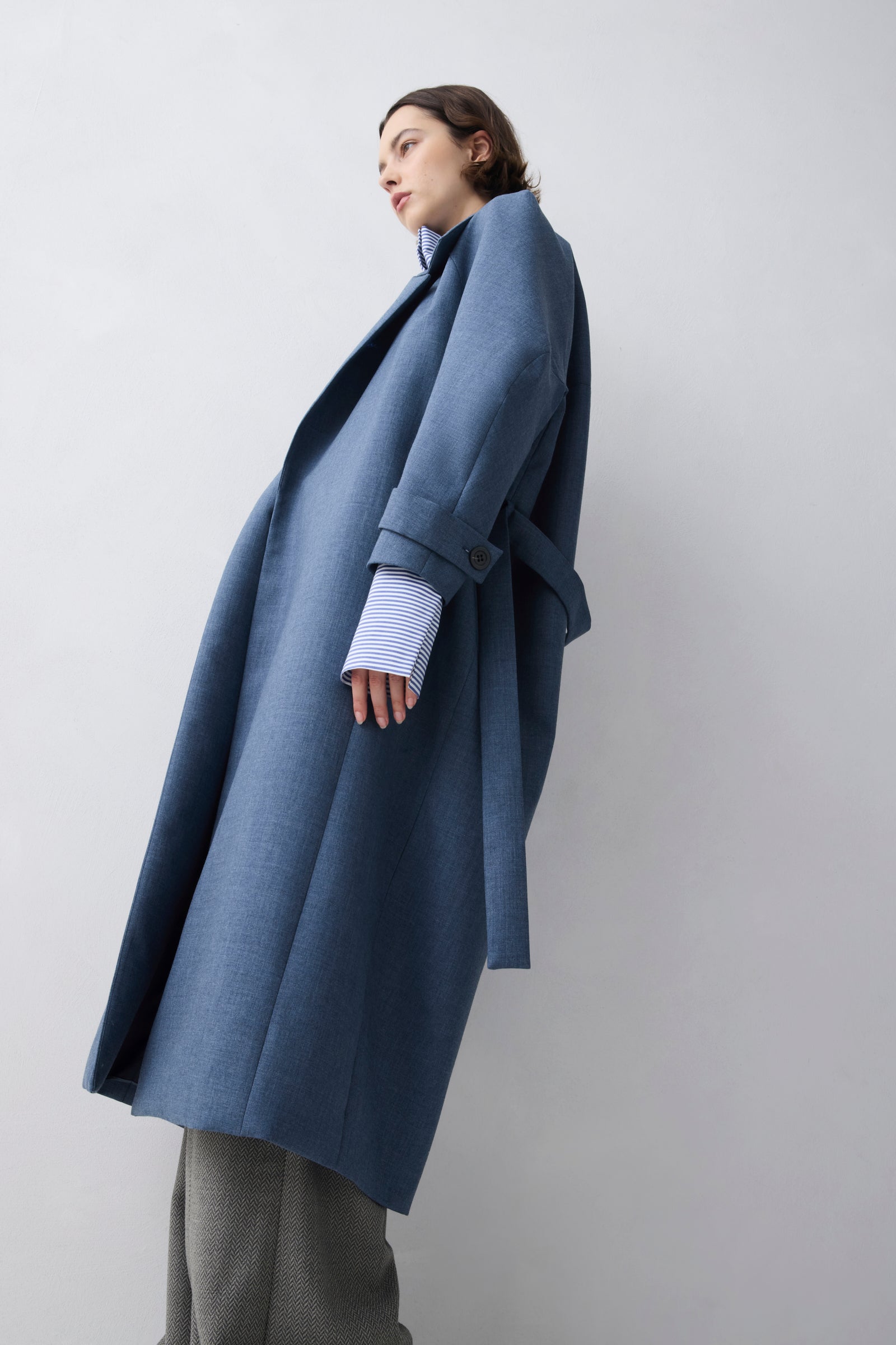 Person wearing a long blue coat on a plain background