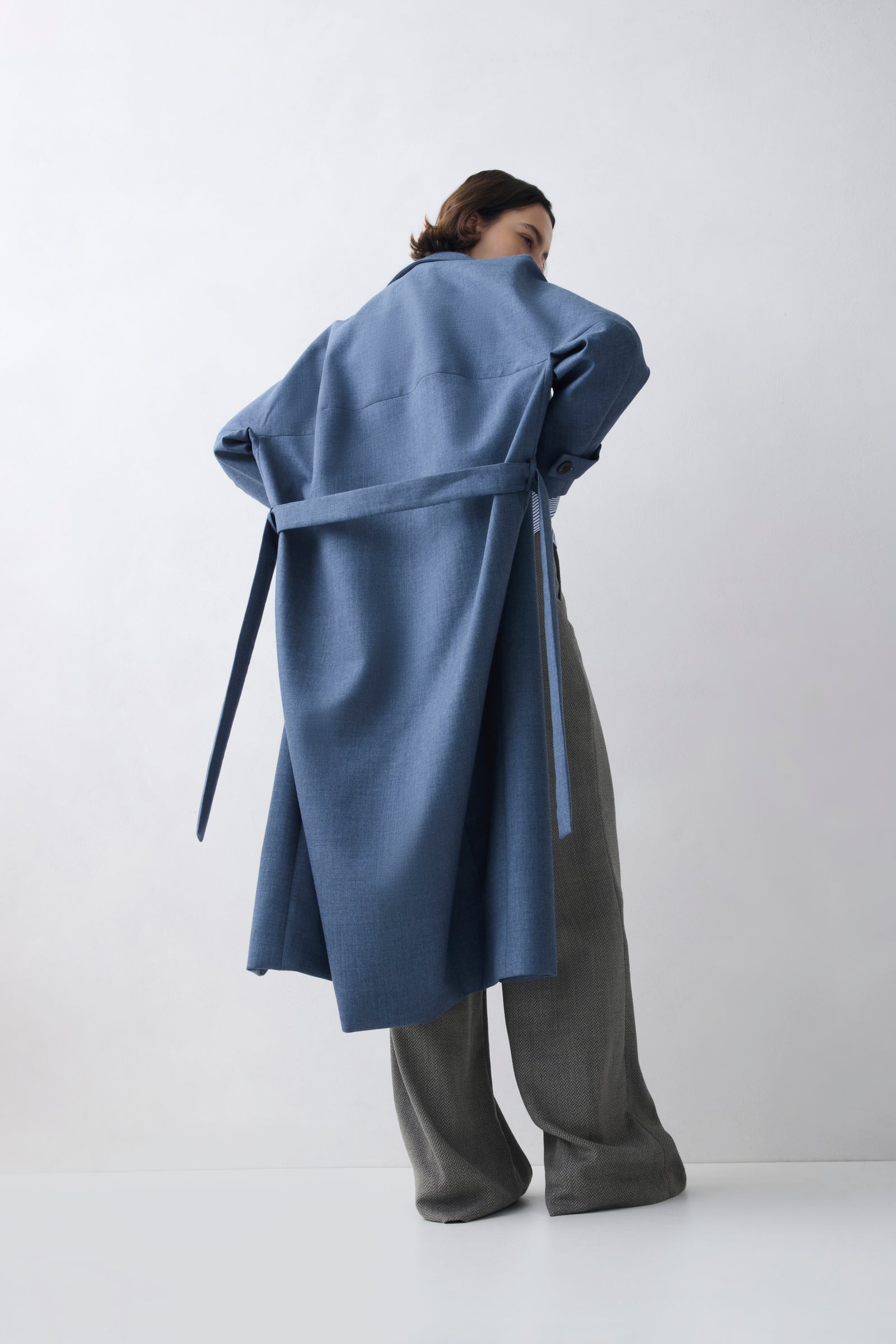 Person wearing a blue coat with a belt on a white background